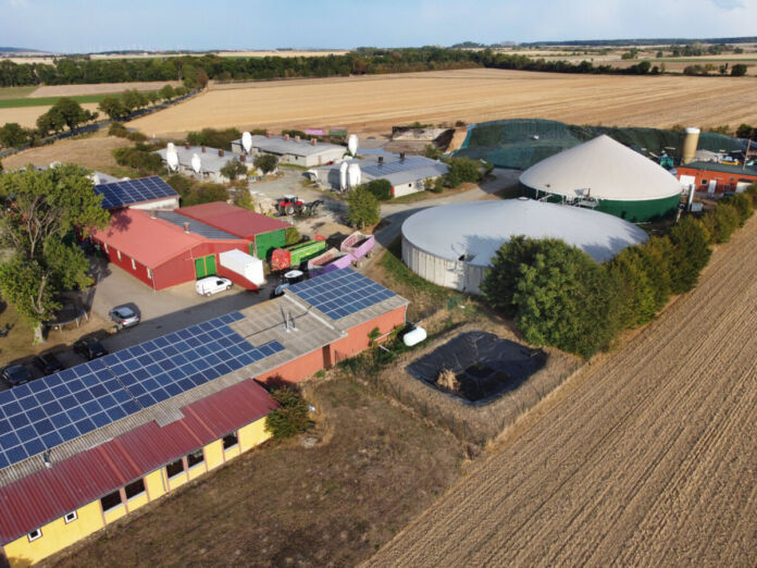 Aus der Luft aufgenommes Bild einer großen Biogsasanlage mit riesigen Silos und vielen Bauernhäusern. Weiterhin gibt es dort viele Ställe und große Felder in der Umgebung.