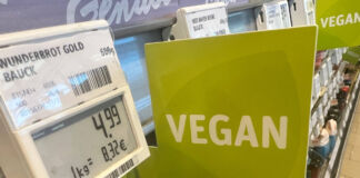 Im Regal eines Supermarktes oder eines Discounters gibt es eine große Auswahl an verschiedenen veganen Produkten. Ein grünes großes Schild mit der Aufschrift "Vegan" weist darauf hin. Man sieht ein Preisschild mit dem Hinweis, dass es sich hier um veganes Brot handelt.