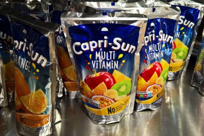 In einem Regal stehen viele Packungen von Capri Sun in den klassischen Sorten Orange und Multi Vitamin. Der Saft ist bei Kindern und Erwachsenen gleichermaßen beliebt.