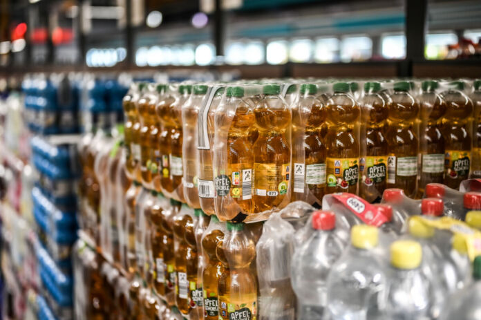 In einer Aldi-Filiale stehen viele Träger unterschiedlicher Getränke auf Paletten gestapelt über- und nebeneinander. Im Vordergrund steht Apfelschorle in kleinen Flaschen. Im Hintergrund stehen verschiedene Sorten von Wasser. Alle Aldi-Filialen sind nun von dem Stopp der Produktion von Getränken betroffen.