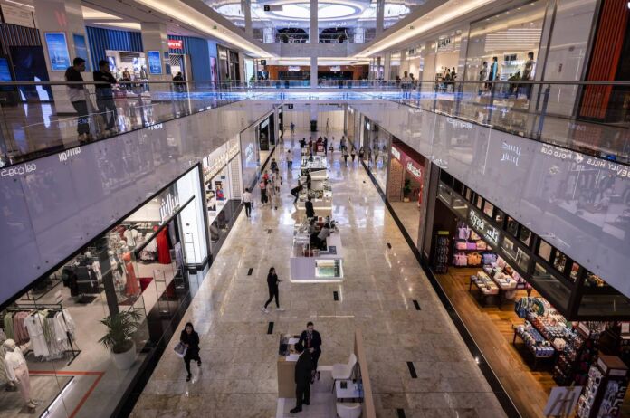 Die Innenaufnahme eines mehrstöckigen Einkaufszentrums. Geschäfte und Boutiquen befinden sich nebeneinander in diesem Kaufhaus. Verschiedene Menschen gehen einkaufen und shoppen. Die Mall ist sehr sauber und modern.