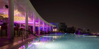 Ein beleuchteter Pool ist bei Nacht in pinkes und blaues Licht getaucht. der Pool gehört zu einem großen Hotel. Das Hotel ist perfekt für einen Luxusurlaub in den Ferien.