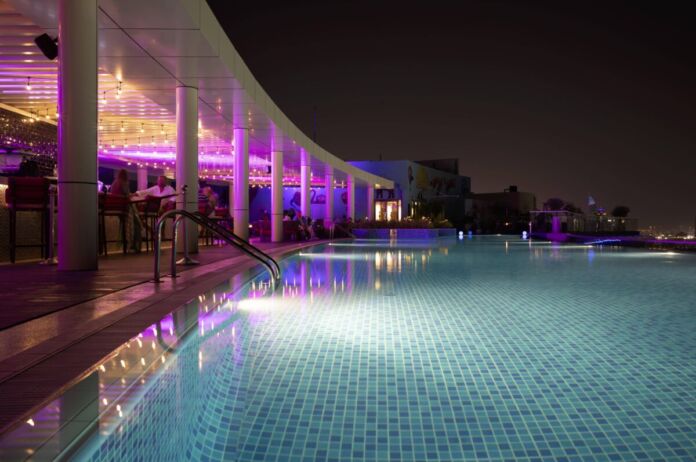 Ein beleuchteter Pool ist bei Nacht in pinkes und blaues Licht getaucht. der Pool gehört zu einem großen Hotel. Das Hotel ist perfekt für einen Luxusurlaub in den Ferien.