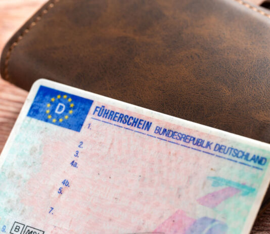 Ein EU-Führerschein der Bundesrepublik Deutschland liegt neben einer braunen Geldbörse aus Leder. Auf dem Führerschein sind keine Eintragungen vorgenommen worden.