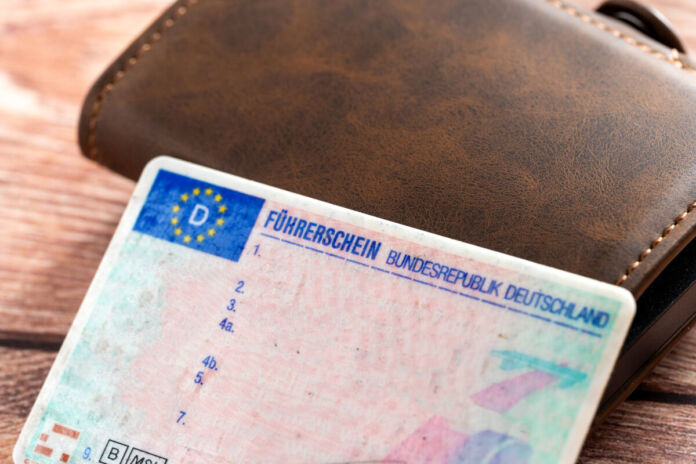 Ein EU-Führerschein der Bundesrepublik Deutschland liegt neben einer braunen Geldbörse aus Leder. Auf dem Führerschein sind keine Eintragungen vorgenommen worden.