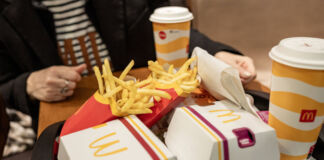 Eine Kundin sitzt bei McDonald's an einem Tisch. Vor ihr steht ein Tablett mit zwei Getränken, Pommes und zwei Burgern.