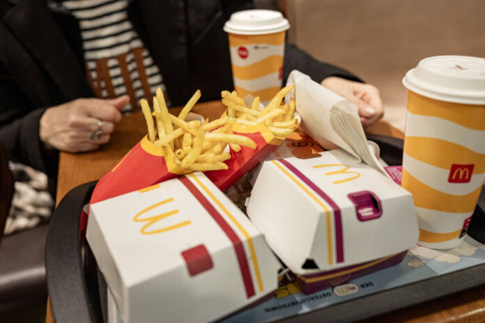 Eine Kundin sitzt bei McDonald's an einem Tisch. Vor ihr steht ein Tablett mit zwei Getränken, Pommes und zwei Burgern.