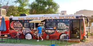 Ein großer bunter Food Truck-Wagen bietet frische Speisen und Getränke zum Mitnehmen an. Hierbei handelt es sich um Pizza und Pasta, leichte Gerichte für den Sommer.