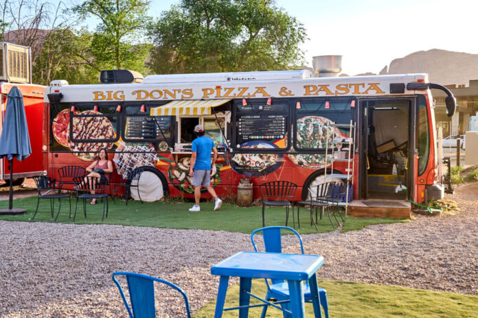 Ein großer bunter Food Truck-Wagen bietet frische Speisen und Getränke zum Mitnehmen an. Hierbei handelt es sich um Pizza und Pasta, leichte Gerichte für den Sommer.