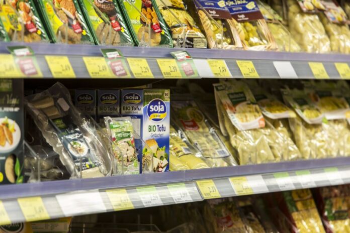 In einem Regal in einem Supermarkt befinden sich viele verschiedene vegane und vegetarische Produkte. Die Kunden haben eine breite Auswahl an Alternativen zu tierischen Produkten.