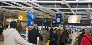 In einem IKEA-Markt stehen viele Menschen an verschiedenen Kassen in einer langen Schlange und warten ungeduldig darauf, dass ihre ausgesuchten Waren abkassiert werden.