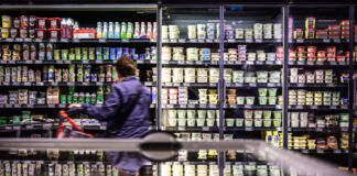 Eine Kunde steht in einem Supermarkt vor einem Kühlregal, in dem sich eine breite Auswahl an verschiedenen Milchprodukten befindet.