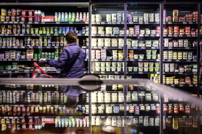 Eine Kunde steht in einem Supermarkt vor einem Kühlregal, in dem sich eine breite Auswahl an verschiedenen Milchprodukten befindet.