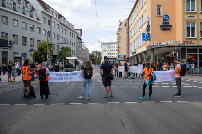 Klimaaktivisten oder Teilnehmer der Klimaaktion blockieren die Straße mit ihren Bannern. Sie tragen orangene Westen und lassen die Autos nicht mehr durch. Es können sich dabei Mitglieder der letzten Generation befinden.