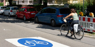 Eine Frau fährt mit dem Fahrrad in einer Fahrradstraße. Am Fahrbahnrand parken verschiedene Autos, diese Fahrzeuge sind stark eingeschränkt, wenn sie auf der Fahrradstraße weiterfahren. Viele Straßen sind für andere Fahrzeuge gesperrt.