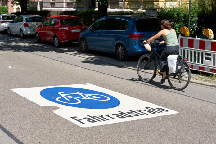 Eine Frau fährt mit dem Fahrrad in einer Fahrradstraße. Am Fahrbahnrand parken verschiedene Autos, diese Fahrzeuge sind stark eingeschränkt, wenn sie auf der Fahrradstraße weiterfahren. Viele Straßen sind für andere Fahrzeuge gesperrt.