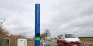 Eine große blaue Säule steht am Rand einer Landstraße, auf der gerade ein VW-Bus fährt. Die blaue Säule erfasst jedes Auto, das an ihr vorbeifährt.