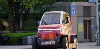 Eins der schmalsten Autos fährt auf einer Straße. Bei dem Stromer handelt es sich um den City Transformer – ein elektrisches faltbares Auto, dessen Größe sich verändern lässt.