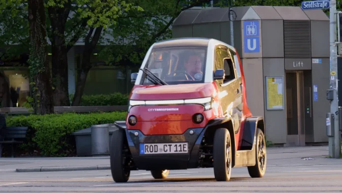 Eins der schmalsten Autos fährt auf einer Straße. Bei dem Stromer handelt es sich um den City Transformer – ein elektrisches faltbares Auto, dessen Größe sich verändern lässt.