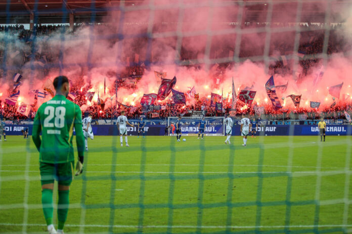 Die Fans zünden im Wildparkstadion Pyrotechnik und erleuchten damit die gesamte Tribüne. Während auf dem Rasen ein Spiel läuft, gibt das Ganze ein gefährliches Bild ab.