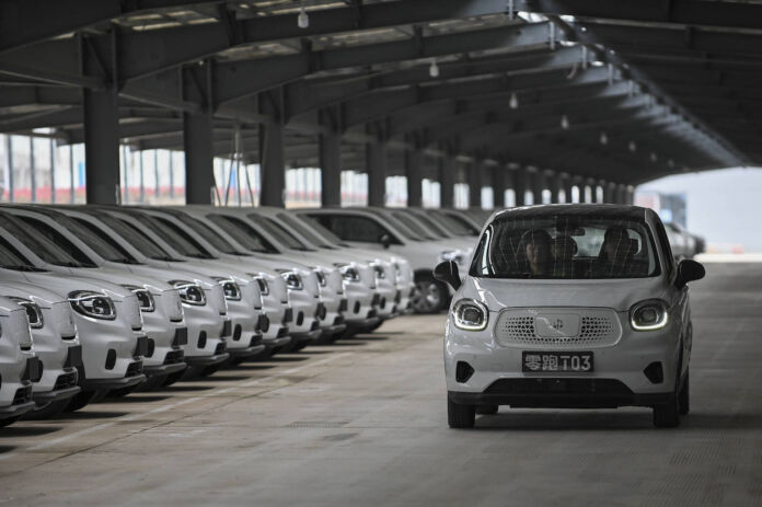 Viele kleine weiße chinesische E-Autos stehen in einer Halle in einer Reihe. Die elektrischen Neuwagen zählen zu den günstigsten überhaupt.