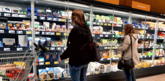 Zwei Frauen beim Einkaufen im Supermarkt stehen vor dem Kühlregal und suchen nach Lebensmitteln. Im Kühlregal sind verschiedene abgepackte Produkte wie Fertiggerichte mit Fisch zu finden.