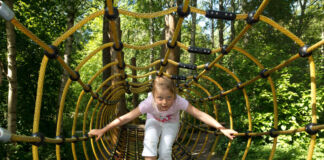 Ein Kind krabbelt durch einen Tunnel aus Seilen. Die Attraktion erinnert an ein Spinnennetz. Es ist ein schönes Ausflugsziel für Kinder im Sommer.