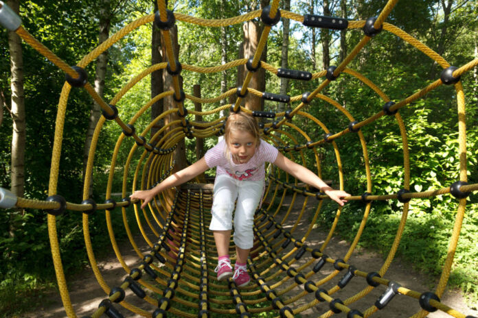 Ein Kind krabbelt durch einen Tunnel aus Seilen. Die Attraktion erinnert an ein Spinnennetz. Es ist ein schönes Ausflugsziel für Kinder im Sommer.