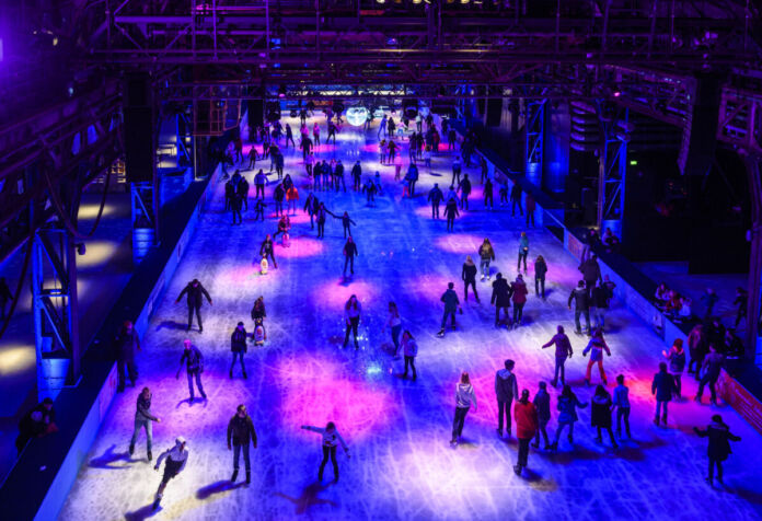 Die Gäste gehen eislaufen in einer Eishalle bei Nacht. Sie tummeln sich in den Eishallen zu einer Eisdisko - es ist dunkel und es leuchtet eine Light Show.