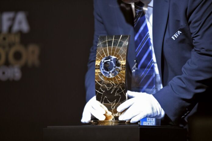 Eine Person stellt den Ballon d'Or auf den Trophäentisch. Er zeichnet den Weltfußballer des Jahres aus, der jedes Jahr neu gewählt wird. Diese Auszeichnung ist besonders wertvoll und wird nur wenigen Fußballern zuteil.