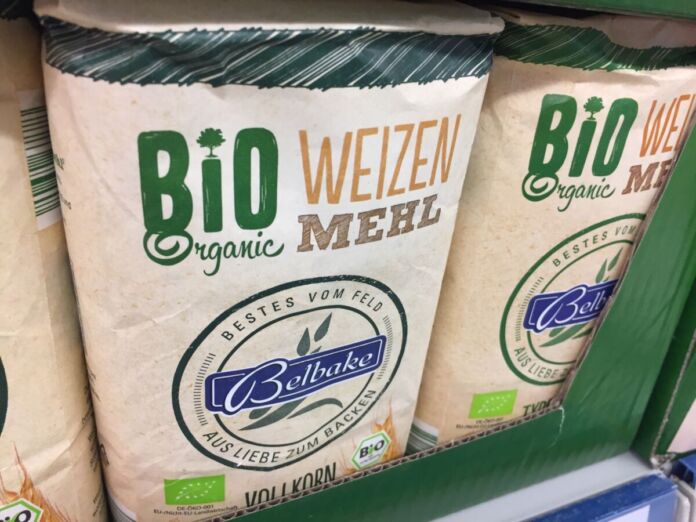 Im Regal eines Discounters oder Supermarktes stehen mehrere Packungen Weizenmehl. Die Beschriftung zeigt, dass es sich um ein Bio-Produkt und um die Eigenmarke eines Discounters oder Supermarktes handelt.