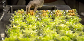 Ein Koch bereitet mehrere Beilagen mit Salat und Gemüse oder Kartoffeln zu. Es handelt sich um vegetarische oder vegane Gerichte, die in einem Restaurant zum Hauptgericht gereicht werden.