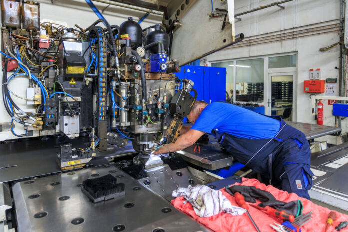 Ein Arbeiter befindet sich in einer Fertigungshalle und bedient eine moderne Maschine. Die Anlage befindet sich in einer Fabrik, in der Produkte in der Industrie hergestellt werden.