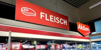 Im Kühlregal eines Supermarktes oder eines Discounters befinden sich viele verschiedene Fleischsorten. Über dem Regal befindet sich ein rotes Schild mit einer weißen Aufschrift "Fleisch". Daneben gibt es ein ebenfalls rotes Schild mit der weißen Aufschrift "Aktion".