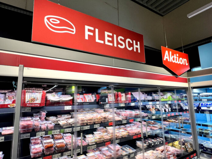 Im Kühlregal eines Supermarktes oder eines Discounters befinden sich viele verschiedene Fleischsorten. Über dem Regal befindet sich ein rotes Schild mit einer weißen Aufschrift "Fleisch". Daneben gibt es ein ebenfalls rotes Schild mit der weißen Aufschrift "Aktion".