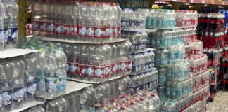 Gestapeltes Wasser in Plastikflaschen in einem Supermarkt. Zur Auswahl steht stilles Wasser und Wasser mit Kohlensäure. Im Hintergrund stehen neben dem Wasser auch Plastikflaschen mit Cola.