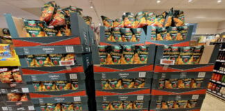 In einem Discounter oder einem Supermarkt sind viele Kartons mit Chips-Tüten übereinander gestapelt. Die Chips sind von einer bekannten Marke. Es gibt verschiedene Sorten.