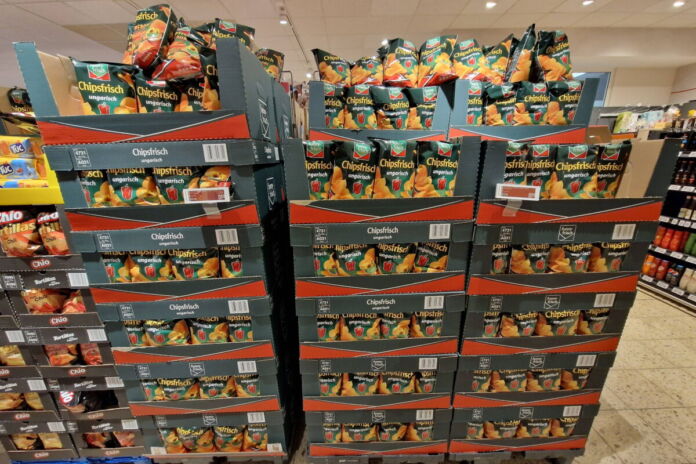 In einem Discounter oder einem Supermarkt sind viele Kartons mit Chips-Tüten übereinander gestapelt. Die Chips sind von einer bekannten Marke. Es gibt verschiedene Sorten.