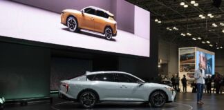 Auf einer Bühne bei einer Autoshow wird ein revolutionäres E-Auto präsentiert mit beeindruckender Technologie und Design. Ein Redner steht auf der Bühne neben dem Fahrzeug und präsentiert es.