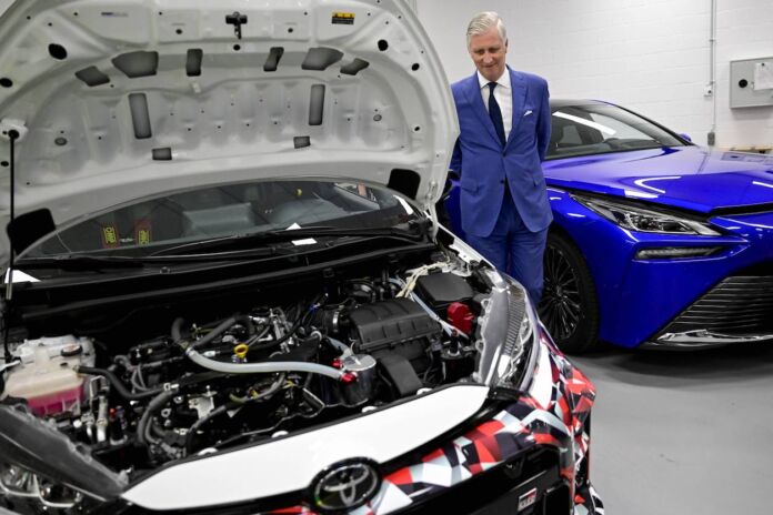 Ein älterer Herr im Anzug steht neben einem Auto von Toyota. Es handelt sich um den belgischen König Philippe, der das technische Zentrum des japanischen Automobilriesen besucht. Die Motorhaube des Wagens ist geöffnet.