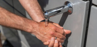 Ein Mann wäscht sich seine Hände unter laufendem Wasser, das aus einem Wasserhahn kommt. Das Wasser stammt aus einem öffentlichen Wasserspender.