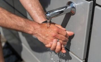 Ein Mann wäscht sich seine Hände unter laufendem Wasser, das aus einem Wasserhahn kommt. Das Wasser stammt aus einem öffentlichen Wasserspender.