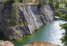 Ein abgelegener Ort in der Natur. Von dem Wald, der aus Tannen besteht, führt eine steile abschüssige Felswand hinunter in einen türkisblauen Fluss.