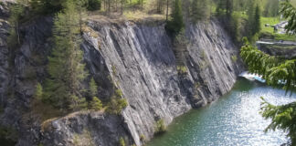 Ein abgelegener Ort in der Natur. Von dem Wald, der aus Tannen besteht, führt eine steile abschüssige Felswand hinunter in einen türkisblauen Fluss.