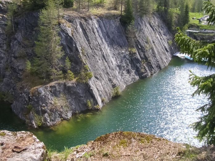 Ein abgelegener Ort in der Natur. Von dem Wald, der aus Tannen besteht, führt eine steile abschüssige Felswand hinunter in einen türkisblauen Fluss.