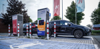 Zwei Elektroautos stehen an einer Ladesäule und werden geladen. Die Parkplätze sind mit einem Extra-Symbol gekennzeichnet. Die beiden anderen Parkplätze sind noch frei.