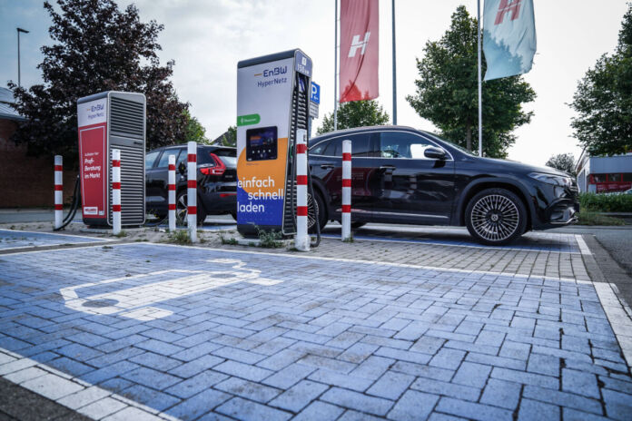 Zwei Elektroautos stehen an einer Ladesäule und werden geladen. Die Parkplätze sind mit einem Extra-Symbol gekennzeichnet. Die beiden anderen Parkplätze sind noch frei.