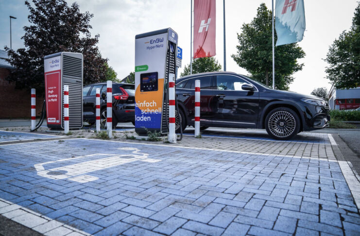 Zwei Elektroautos stehen an einer Ladesäule und werden geladen. Die Parkplätze sind mit einem Extra-Symbol gekennzeichnet. Die beiden anderen Parkplätze sind noch frei.