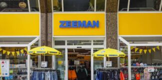 Eine Filiale der niederländischen Einzelhandelskette "Zemann" im typischen gelb-blauen Design. Vor dem Geschäft hängen Jeans und andere Hosen unter Schirmen. Preisschilder locken mit Angeboten.