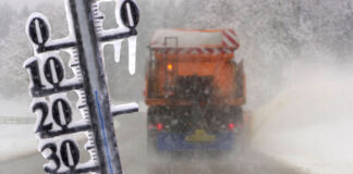 Blick auf eine vereiste Straße mit einem Lkw, der sich seinen Weg durch einen Schneesturm bahnt. Davor erkennt man ein Thermometer, welches ebenfalls mit Eis bedeckt ist. Es ist offenbar tiefster Winter und sehr kalt.